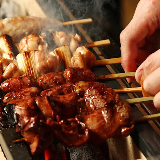 炭火の前で焼き鳥を返す調理人の手元と焼き網